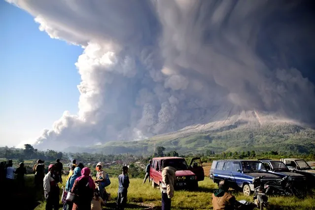 People watch as Mount Sinabung erupts in Karo, North Sumatra, Indonesia, Tuesday, March 2, 2021. The 2,600-meter (8,530-feet) volcano spewed materials a few thousand meters (yards) into the sky and deposited ash on nearby villages. (Photo by AP Photo/Stringer)