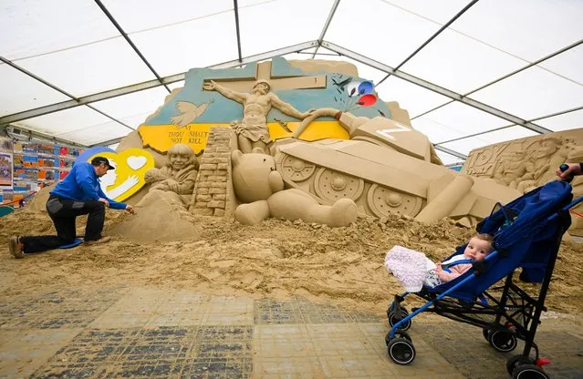 Tourists pass Slava Borecki's sculpture as he puts the finishing touches, on April 28, 2022 in Weymouth, England. Award-winning Ukrainian Sand Sculptor Slava Borecki's emotive sand sculpture is on display at Weymouth's SandWorld Sculpture Park as he makes a plea for peace across the world. (Photo by Finnbarr Webster/Getty Images)