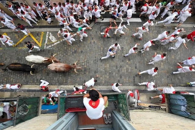A resident watch from their balcony as participants run with bulls during the first “encierro” (bull-run) of the San Fermin festival in Pamplona, northern Spain, on July 7, 2023. Thousands of people every year attend the week-long festival and its famous “encierros”: six bulls are released at 8:00 a.m. evey day to run from their corral to the bullring through the narrow streets of the old town over an 850 meters (yard) course while runners ahead of them try to stay close to the bulls without falling over or being gored. (Photo by Ander Gillenea/AFP Photo)