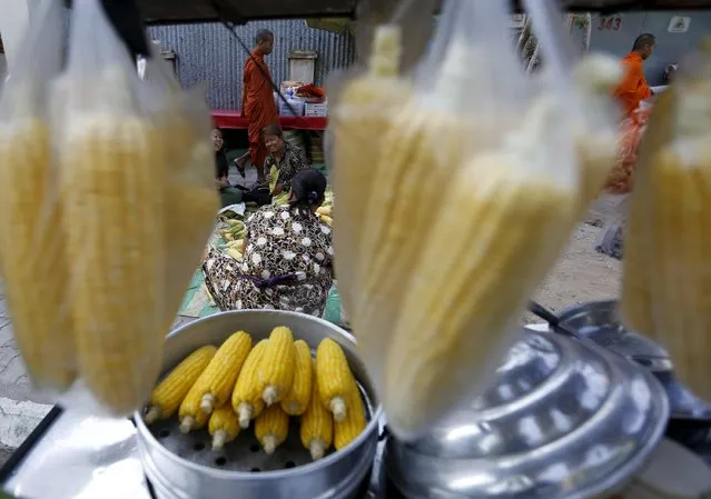 Buddhist monks walk pass as vendors clean corn cobs before steaming them to be sold in a street in central Phnom Penh December 30, 2015. (Photo by Samrang Pring/Reuters)