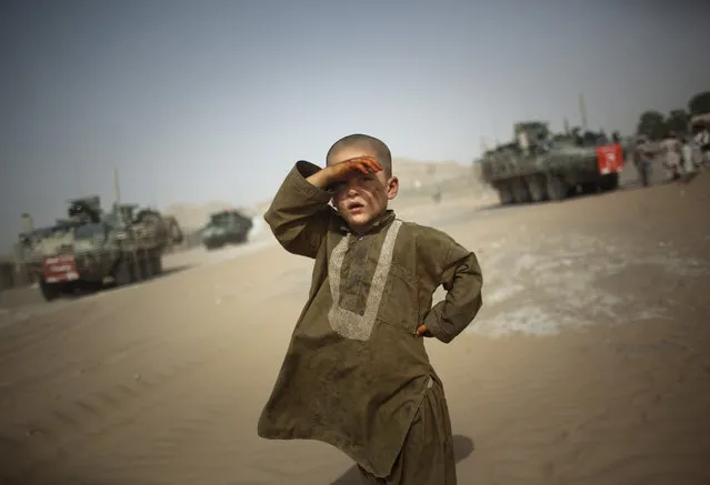 A child looks on as military vehicles of 5th Striker Brigades drive past his village on the outskirts of Spin Boldak, about 100 kilometers (63 miles, File) southeast of Kandahar, Afghanistan, on Auguast 6, 2009. (Photo by Emilio Morenatti/AP Photo/File)