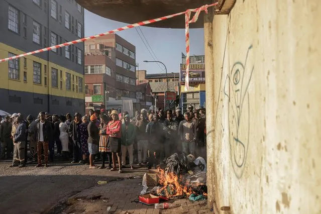 People standing at a bonfire look on as unseen firefighters work at the scene of a fire in a building in Johannesburg on August 31, 2023. At least 20 people have died and more than 40 were injured in a fire that engulfed a five-storey building in central Johannesburg on August 31, 2023, the South African city's emergency services said. (Photo by Michele Spatari/AFP Photo)