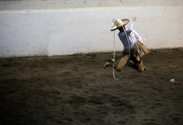 In this February 26, 2015 photo, Charro Carlos Maurer, from Puebla, practices his lasso skills ahead of the roping events, during a charreada in Mexico City. In team roping, charros must lasso both the neck and the hind legs of a bull, while in horse roping a charro on foot must capture a wild horse by roping its front legs. Extra points are awarded for rope tricks. (Photo by Rebecca Blackwell/AP Photo)