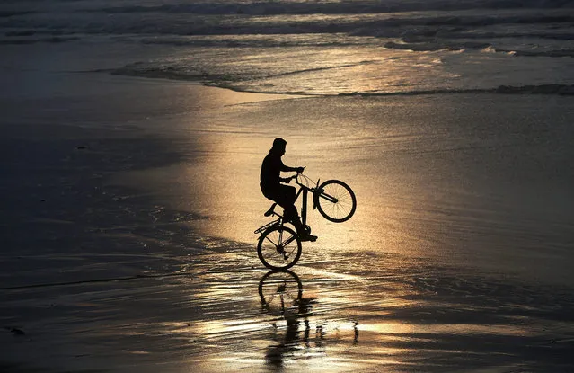 A Palestinian boy rides his bicycle at the beach at sunset during rainy weather in the Gaza Strip on, 03 January 2016. (Photo by Mohammed Saber/EPA)
