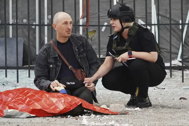 A police officer, right, comforts a man as he holds the hand of a relative killed in Russian shelling in Kharkiv, Ukraine, Wednesday, July 20, 2022. (Photo by Andrii Marienko/AP Photo)