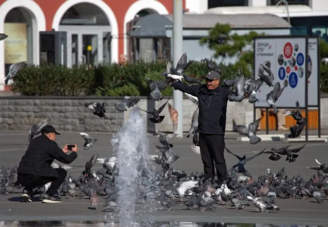 A Chinese tourist poses with pigeons in Vladivostok, Russia on October 16, 2023. (Photo by Tatiana Meel/Reuters)