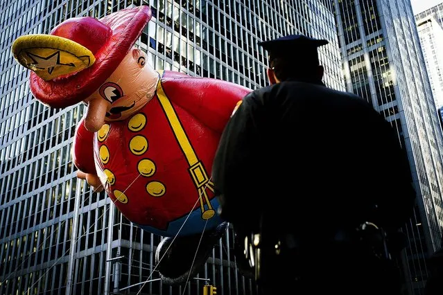 A police officer stands on Sixth Avenue as a giant fireman balloon passes. (Photo by John Minchillo/Associated Press)