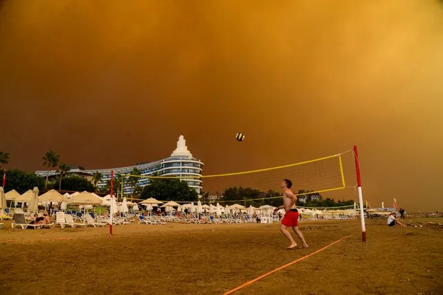 Dark smoke drifts over a hotel complex during a massive forest fire which engulfed a Mediterranean resort region on Turkey's southern coast near the town of Manavgat, on July 29, 2021. At least three people were reported dead on July 29, 2021 and more than 100 injured as firefighters battled blazes engulfing a Mediterranean resort region on Turkey's southern coast. Officials also launched an investigation into suspicions that the fires that broke out Wednesday in four locations to the east of the tourist hotspot Antalya were the result of arson. (Photo by Ilyas Akengin/AFP Photo)