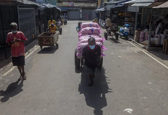 Sri Lankan daily waged laborers transport a cart load of imported garlic during restrictions imposed to curb the spread of the coronavirus at a wholesale market place in Colombo, Sri Lanka on June 16, 2021. (Photo by Eranga Jayawardena/AP Photo)