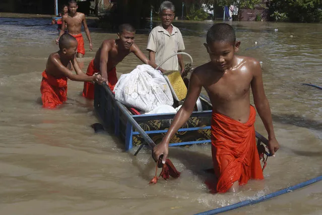 Buddhist monks make their way through a flooded street with the belongings of their pagoda on a cart, following recent rains, near Wat Kampong Kampong Kdol pagoda outside Phnom Penh , Cambodia, Tuesday, October 26, 2021. (Photo by Heng Sinith/AP Photo)