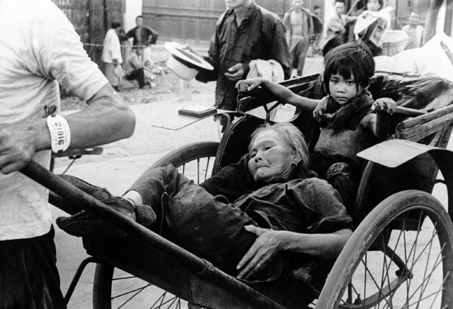 This is the real horror of war. The aged Chinese woman, badly hurt after a Japanese bombing raid on the city of Shanghai, is taken through the streets in a rickshaw to receive first aid treatment in China, on September 27, 1937. Her face is distorted with pain, and the ragged, dirty youngster in the back is wondering, perhaps, what all this death and pain can mean. (Photo by AP Photo)