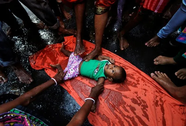 Hindu devotees touch a baby with their feet as part of a ritual to bless him during a religious procession held to mark the Gajan festival in Kolkata, India, April 13, 2019. (Photo by Rupak De Chowdhuri/Reuters)