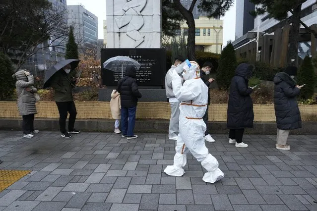 A medical workers passes by people as they wait for the coronavirus testing outside a public health center in Seoul, South Korea, Wednesday, December 15, 2021. Halting its steps toward normalcy, South Korea will clamp down on social gatherings and cut the hours of some businesses to fight a record-breaking surge of the coronavirus that has led to a spike in hospitalizations and deaths. (Photo by Ahn Young-joon/AP Photo)