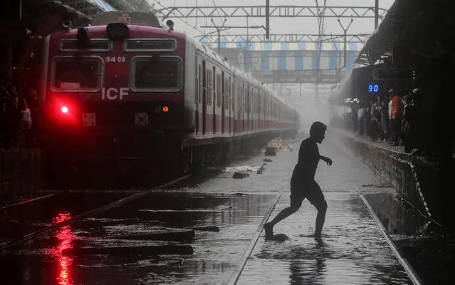 A commuter crosses waterlogged railway tracks as a suburban train is seen parked at a railway station after its services were suspended during heavy monsoon rains in Mumbai, July 2, 2019. (Photo by Francis Mascarenhas/Reuters)