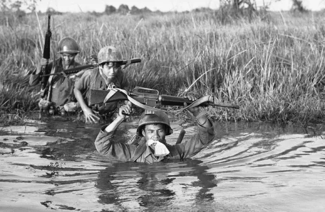 In this March 11, 1972 file photo, a South Vietnamese soldier holds his personal belongings in a plastic bag between his teeth as his unit crosses a muddy Mekong Delta stream in Vietnam near the Cambodian border. His unit was charged with stemming Communist infiltration from Cambodia into South Vietnam in the heavily populated Mekong Delta area. (Photo by Nick Ut/AP Photo)