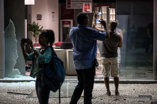 People take pictures of the entrance of a bank vandalized by protesters during a national strike against the government' s social welfare reform bill which seeks to extend the time of contributions and raise the minimum age required to obtain full retirement benefits, in Rio de Janeiro, Brazil, on March 15, 2017 Since replacing leftist President Dilma Rousseff in Congress in 2016, President Michel Temer has been pushing for an adjustment program aimed at regaining market confidence and reactivating the country' s economy, in recession for more than two years. (Photo by Mauro Pimentel/AFP Photo)