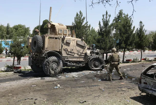A NATO soldier walks near a damaged vehicle at the site of a suicide attack on a NATO convoy in Kabul, Afghanistan, Tuesday, June 30, 2015. It comes a week after an audacious attack on the nation's parliament, which highlighted the ability of insurgents, who have been fighting to overthrow the Kabul government for almost 14 years, to enter the highly fortified capital to stage deadly attacks. (Photo by Rahmat Gul/AP Photo)