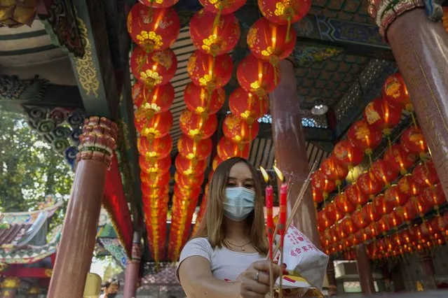 A woman holds joss sticks praying for good fortune on the eve of the Lunar New Year at Tai Hong Kong Shrine in Bangkok, Thailand, Monday, January 31, 2022. The new year celebrations according to the lunar calendar will take place on Feb. 1. (Photo by Sakchai Lalit/AP Photo)
