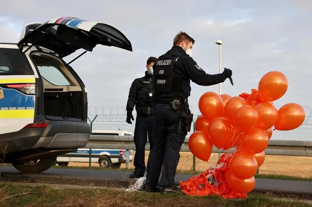 A German police officer pops confiscated balloons, following a “Letzte Generation” (Last Generation) activist's attempt to release balloons to interrupt air traffic at Berlin Brandenburg Airport to protest against food waste and for an agricultural change to reduce greenhouse gas emissions, in Berlin, Germany, February 25, 2022. (Photo by Christian Mang/Reuters)