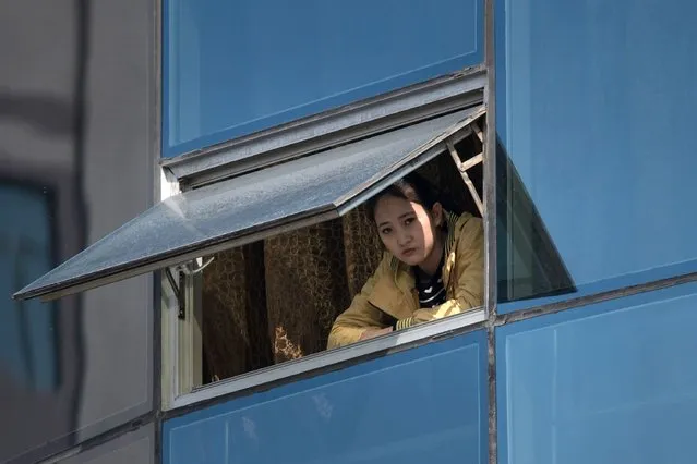 A woman watches from a window as competitors run along Mirae Scientists Street during the Pyongyang Marathon in Pyongyang on April 9, 2017. Hundreds of foreigners lined up in Pyongyang's Kim Il-Sung Stadium on April 9 for the city's annual marathon, the highlight of the tourism calendar in isolated North Korea. (Photo by Ed Jones/AFP Photo)