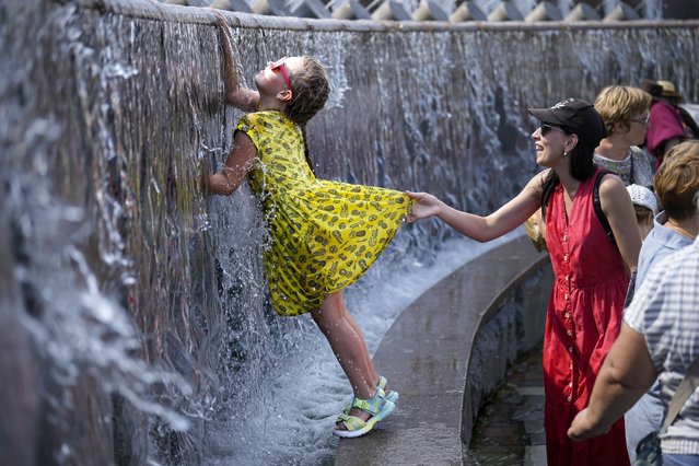 A girl cools herself in a fountain at Manezhnaya Square near the Kremlin Wall in Moscow, Russia, Tuesday, July 2, 2024. Warm weather has settled in Moscow with a temperature of 32 Celsius, (89,6 Fahrenheit) and will increase in the coming days. (Photo by Alexander Zemlianichenko/AP Photo)