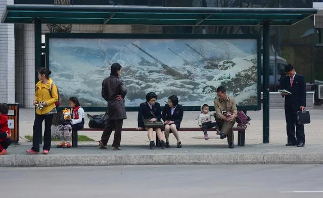 Schoolgirls and families wait for a bus under posters showing North Korean artillery. (Photo by Gavin John/Mediadrumworld.com)