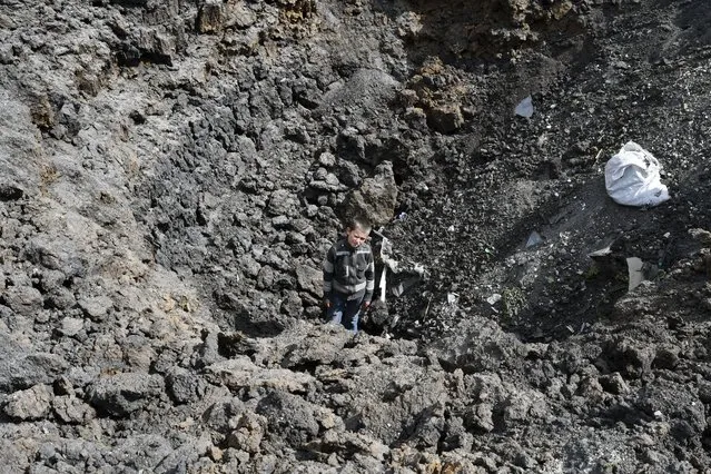 Maxim stands in the crater of an explosion after Russian shelling next to the Orthodox Skete in honor of St. John of Shanghai in Adamivka, near Slovyansk, Donetsk region, Ukraine, Tuesday, May 10, 2022. (Photo by Andriy Andriyenko/AP Photo)