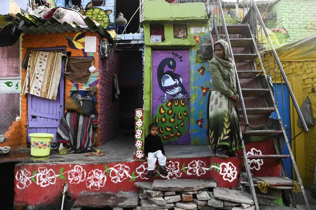 A woman and a child wait in front of a home adorned with murals painted by artists from “Delhi Street Art” group at the Raghubir Nagar slum in New Delhi on December 2, 2019. (Photo by Sajjad Hussain/AFP Photo)