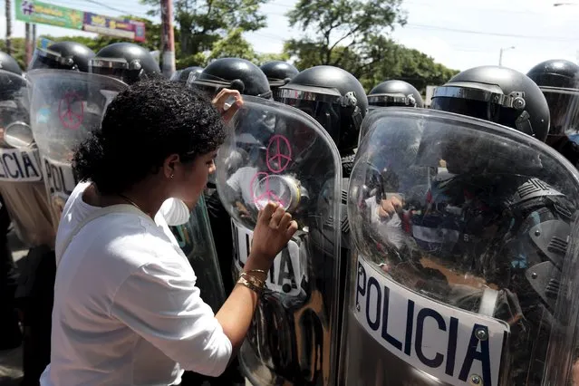 An opposition supporter draws peace signs on the shield of a riot police officer during a protest in front of the Supreme Electoral Council (CSE) building in Managua, Nicaragua August 5, 2015. The protesters said they were demonstrating to demand fairer elections in the country next year. (Photo by Oswaldo Rivas/Reuters)