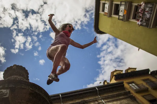 A reveler jumps from a fountain onto the crowd below, after the launch of the “Chupinazo” rocket, to celebrate the official opening of the 2014 San Fermin fiestas in Pamplona, Spain, Sunday, July 6, 2014. Revelers from around the world turned out here to kick off the festival with a messy party in the Pamplona town square, one day before the first of eight days of the running of the bulls glorified by Ernest Hemingway's 1926 novel “The Sun Also Rises”. (Photo by Andres Kudacki/AP Photo)