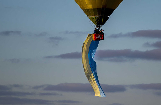 A hot-air balloon decorated with a Ukrainian national flag floats in the air over Vilnius during the protest against the Russian invasion of Ukraine, in Vilnius, Lithuania, Saturday, March 5, 2022. More than 1 million people have fled Ukraine following Russia's invasion in the swiftest refugee exodus in this century, the United Nations said Thursday. (Photo by Mindaugas Kulbis/AP Photo)