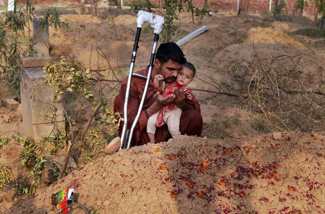 Mohammed Tofeeq holds his 10-month-old daughter, Gulshan Tofeeq, while he prays at the grave of his wife Muqadas Tofeeq, who local police say was killed by her mother, in Butrawala village on the outskirts of Gujranwala, Pakistan,  June 18, 2016. (Photo by K.M. Chaudary/AP Photo)