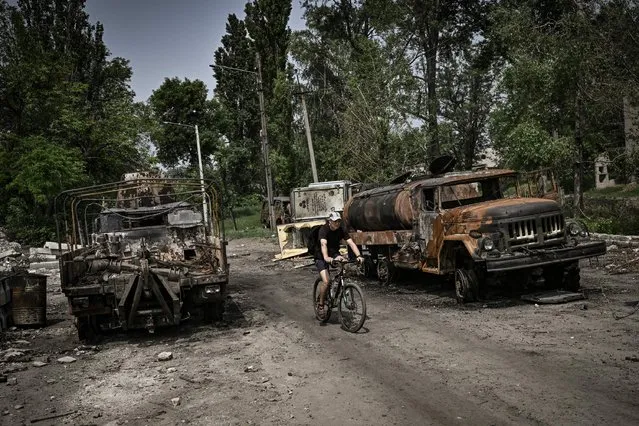 A man rides his bicycle between two destroyed military trucks in the city of Lysychansk, eastern Ukrainian region of Donbas, on June 11, 2022. (Photo by Aris Messinis/AFP Photo)