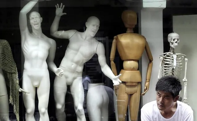 A man sits in front of mannequins on display at a shop in Shanghai, China on June 8, 2012