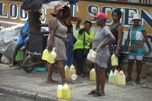 Women show their discomfort as they are being photographed selling contraband gasoline in plastic gallons jugs on a street in Port-au-Prince, Haiti, Thursday, July 14, 2022. (Photo by Joseph Odelyn/AP Photo)