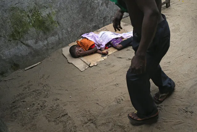 A man walks past a sick Saah Exco, 10, in a back alley of the West Point slum on August 19, 2014 in Monrovia, Liberia. According to communitey organizer John Saah Mbayoh, Saah's mother died of suspected but untested Ebola in West Point before he was brought to the isolation center the evening of August 13. He came with his brother, Tamba, 6, aunt Ma Hawa, and cousins. His brother died on August 15 at the center. Saah fled the center the August 15 with several other patients before it was overrun on August 16 by a mob. (Photo by John Moore/Getty Images)