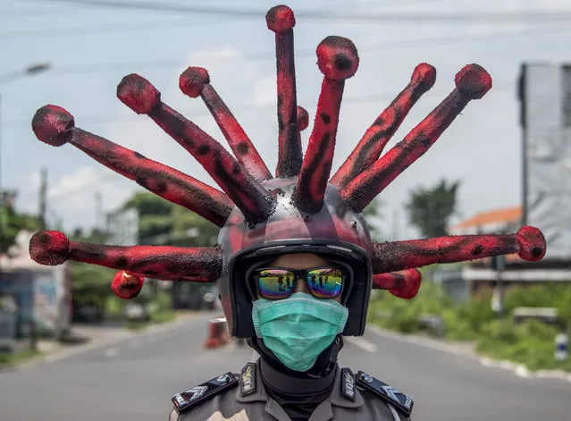 An Indonesian police officer wearing a Covid-19 coronavirus themed helmet conducts a campaign and disinfects motorists' vehicles in Mojokerto, East Java on April 3, 2020. (Photo by Juni Kriswanto/AFP Photo)