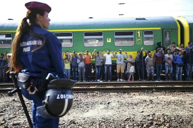 A police officer stands guard as migrants stage a protest in front of a train at Bicske railway station, Hungary, September 4, 2015. Hundreds of migrants, many of them refugees from the Syrian war, woke after a night spent on a packed train stranded at a railway station west of Budapest, refusing to go to a nearby camp to process asylum seekers. The train had left Budapest on Thursday morning after a two-day standoff at the city's main railway station as police barred entry to some 2,000 migrants. (Photo by Leonhard Foeger/Reuters)