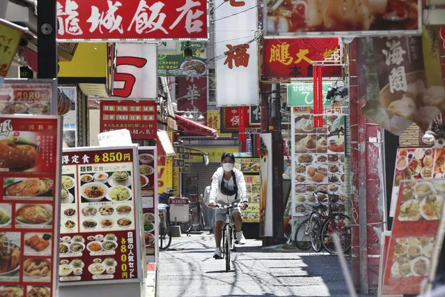 A man wearing a face mask to protect against the spread of the new coronavirus cycles through China Town in Yokohama, near Tokyo, Friday, May 8, 2020. Prime Minister Shinzo Abe announced that Japan extend a state of emergency until end of May. (Photo by Koji Sasahara/AP Photo)