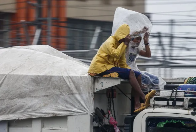 Workers protect themselves from rain while riding atop a garbage truck in Quezon City, Metro Manila, Philippines, 29 October 2022. (Photo by Rolex Dela Pena/EPA/EFE)