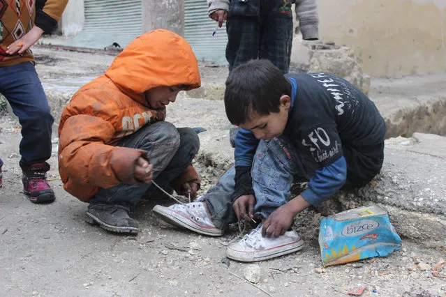 Two children were working in the collection of plastic because of poverty, one of them sat on the sidewalk for linking his shoes and helped his friend, who works with him in Aleppo, Syria on August 19, 2016. (Photo by Basem Ayoubi/ImagesLive via ZUMA Wire)