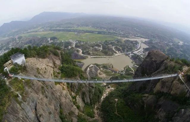 Tourists walk on a suspension bridge made of glass at the Shiniuzhai National Geological Park on September 24, 2015 in Pingjiang County, China. The 300-meter-long glass suspension bridge, with a maximum height of 180 meters, opened to the public on Thursday. (Photo by ChinaFotoPress/ChinaFotoPress via Getty Images)