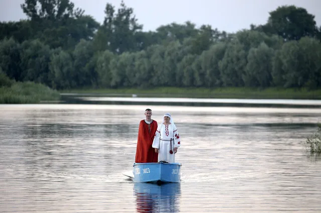 A couple in ethnic costumes stand in a boat during Ivan Kupala Day celebrations held by the Pripyat River in the town of Turauin Gomel Region, Belarus on July 6, 2020. (Photo by Natalia Fedosenko/TASS)