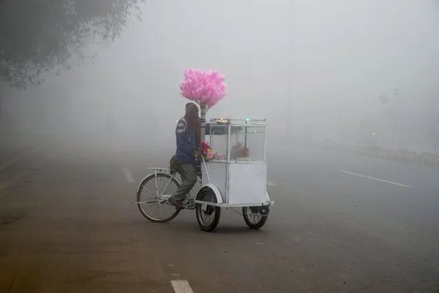 A cotton candy seller waits for customers on a road as heavy fog reduces visibility in Lahore, Pakistan, Monday, January 2, 2023. (Photo by K.M. Chaudary/AP Photo)