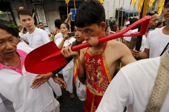 A devotee of the Chinese Bang Neow shrine with a shovel pierced through his cheek walks during a procession celebrating the annual vegetarian festival in Phuket, Thailand October 18, 2015. (Photo by Jorge Silva/Reuters)
