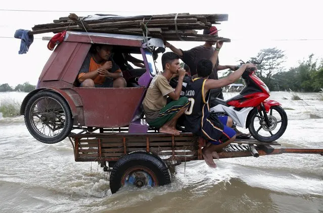 A tricycle and residents are pulled on a farm tractor trailer along a flooded highway in Zaragoza, Nueva Ecija in northern Philippines October 20, 2015, after the province was hit by Typhoon Koppu. (Photo by Erik De Castro/Reuters)