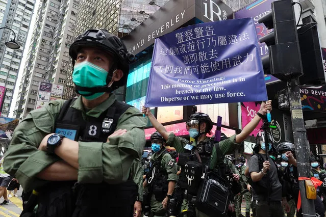 A police officer displays a warning banner on China's National Day in Causeway Bay, Hong Kong, Thursday, October 1, 2020. A popular shopping district in Causeway Bay saw a heavy police presence on the National Day holiday despite low protester turnout. (Photo by Vincent Yu/AP Photo)