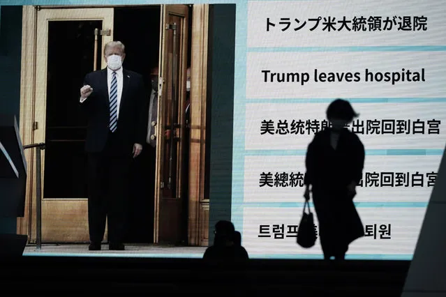 People walk past a screen showing the news report that President Donald Trump has left a hospital to return to the White House after receiving treatments for COVID-19, Tuesday, October 6, 2020, in Tokyo. (Photo by Eugene Hoshiko/AP Photo)