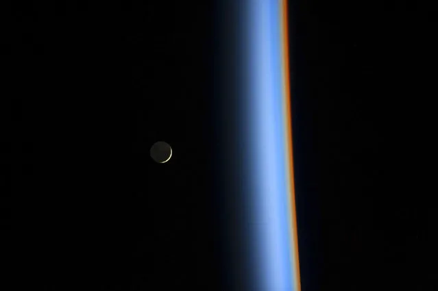 A crescent moon rises over the cusp of the Earth's atmosphere in this picture taken by Japan Aerospace Exploration Agency astronaut Koichi Wakata onboard the International Space Station on February 1, 2014. Distinct colors are visible because the dominant gases and particles in each layer of the atmosphere act as prisms, filtering out certain colors of light. (Photo by Reuters/NASA)
