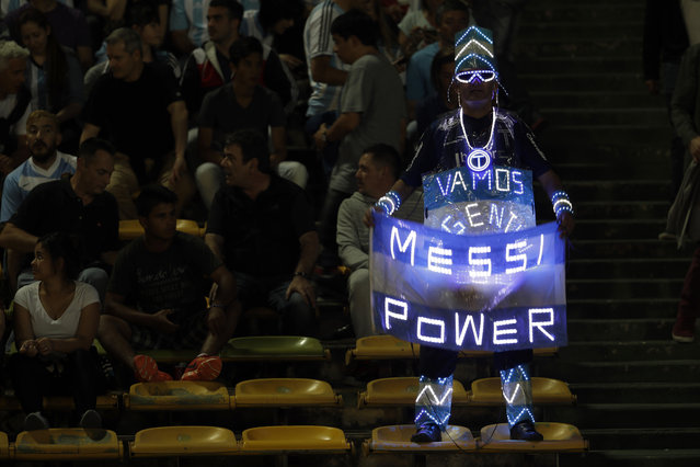 An Argentina fan holds a national flag with a lighted sign in support of star player Lionel Messi, prior a 2018 World Cup qualifying soccer match against Paraguay, in Cordoba, Argentina, Tuesday, October 11, 2016. (Photo by Natacha Pisarenko/AP Photo)